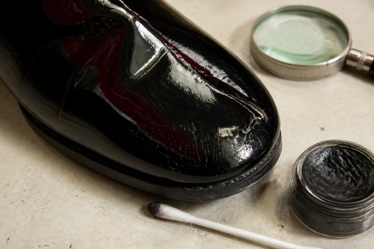Réparer chaussures vernies craquelées : chaussure noire, loupe et kit, avec microfissures et éclats visibles.