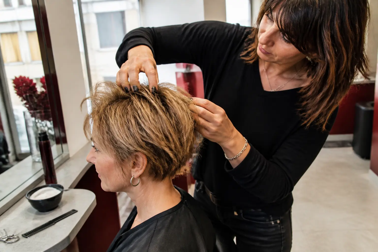 Coupe courte cheveux fins et clairsemés en salon parisien, coiffeuse appliquant un produit texturisant aux racines.